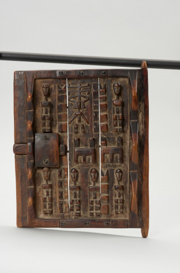 drzwi do spichlerza - Ujęcie z przodu; Drewniane kwadratowe drzwi pokryte płaskorzeźbami postaci ludzkich i zwierząt, które posiadają formę zgeometryzowaną. Drzwi obramowane listwami. Pozostała powierzchnia podzielona na trzy pionowe pasy. Na każdym pionowo umieszczone płaskorzeźby.