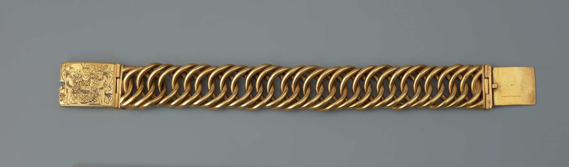 bransoleta z sarkofagu księcia Franciszka I (1577 - 1620) - Ujęcie z tyłu. Bransoleta wykonana ze skręconych, przenikających się ogniw, w tzw. splocie pancerzowym. Na prostokątnych zapinkach dziewięciopolowy herb Księstwa Pomorskiego trzymany przez dzikich mężów, pierwotnie emaliowany. Na spodzie klamry ryta inskrypcja, pierwotnie emaliowana: V.G.G. / CLARA / G.Z.B.V.L. / H.Z.S.Pō /15.96. Na bocznych ściankach wykonana w tej samej technice inskrypcja: V.G.G. FRANTZ / H.Z.S.Pom.