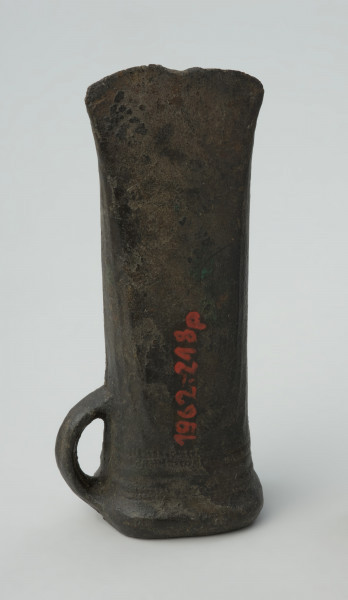 topór, siekiera - Ujęcie tyłu w pionie. Siekierka brązowa z tulejką i dużym uszkiem, dekorowana żeberkowaniem i karbami przy wylocie tulejki.