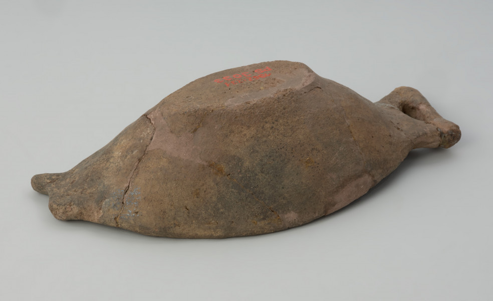 naczynie - Ujęcie spodu z prawego boku. Płytka miseczka o oryginalnej formie, przypominającej kształtem rybę. Powierzchnia naczynia jest niezbyt starannie gładzona, barwa w tonacji szaro-brunatnej.