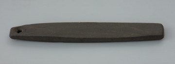 osełka kamienna - Ujęcie z przodu. Osełka ma podłużną, sztabkowatą formę o owalnym kształcie z dwoma zaokrąglonymi końcami. Na wysokości jednego z zakończeń znajduje się skośny otwór przelotowy wywiercony czubkiem noża. Przez dziurę możliwe było przewleczenie rzemienia lub sznurka służącego przytroczeniu osełki do skórzanego paska lub zawieszeniu jej na szyi. Przedmiot ma dwie płaskie powierzchnie pracujące, z czego wyłącznie jedna nosi wyraźne ślady po intensywnym użytkowaniu. Krawędzie są starannie wyprofilowane pod kątem prostym.