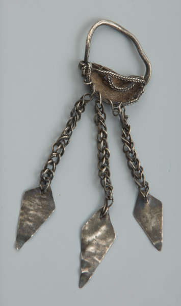 Zausznica srebrna z kolistego w przekroju drucika uformowanego w kabłąk. - Ujęcie z tyłu. Zausznica srebrna z kolistego w przekroju drucika uformowanego w kabłąk o jednym końcu zwężonym i uciętym. W dolnej części drucik jest wykuty w półkolistą blaszkę zakończoną zwinięciem w uszko. Kabłąk jest lekko odkształcony, a krawędzie blaszki są wzmocnione ażurowym pasmem, opracowanego młotkiem drucika wygiętego zygzakowato. Na ażurowe pasma nałożony jest łańcuszek, wykonany z kilku skręconych drucików, którego koniec owinięto wokół uszka. By wzmocnić dolną krawędź blaszki przymocowano do niej trzy łańcuszki ze zginanych wpół ósemkowatych ogniwek. W ostatnim ogniwie każdego z nich zamocowano niezdobione blaszki w kształcie deltoidów z dziurkami w górnych częściach.