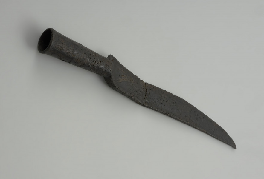 nóż, broń kolna - Ujęcie z góry przodu skosem w prawą stronę. Niezdobiony nóż z brązu z tulejkowatą rękojeścią.