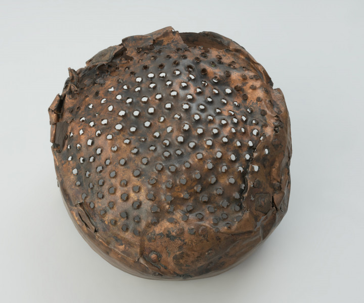 Cedzak ze stopu miedzi - Ujęcie spodu cedzaka. Cedzak ze stopu miedzi o owalnym kształcie z dwoma trójkątnymi uchami.