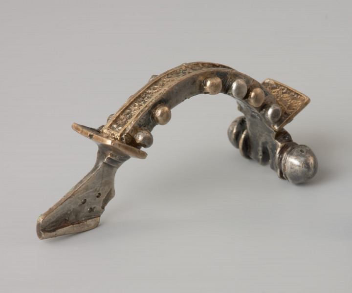 Ujęcie z tyłu. Srebrna zapinka z kabłąkiem zdobionym złotymi kulkami.