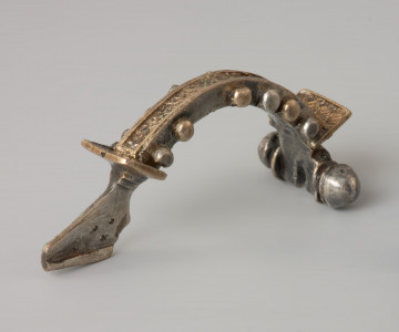 Ujęcie z tyłu. Srebrna zapinka z kabłąkiem zdobionym złotymi kulkami.