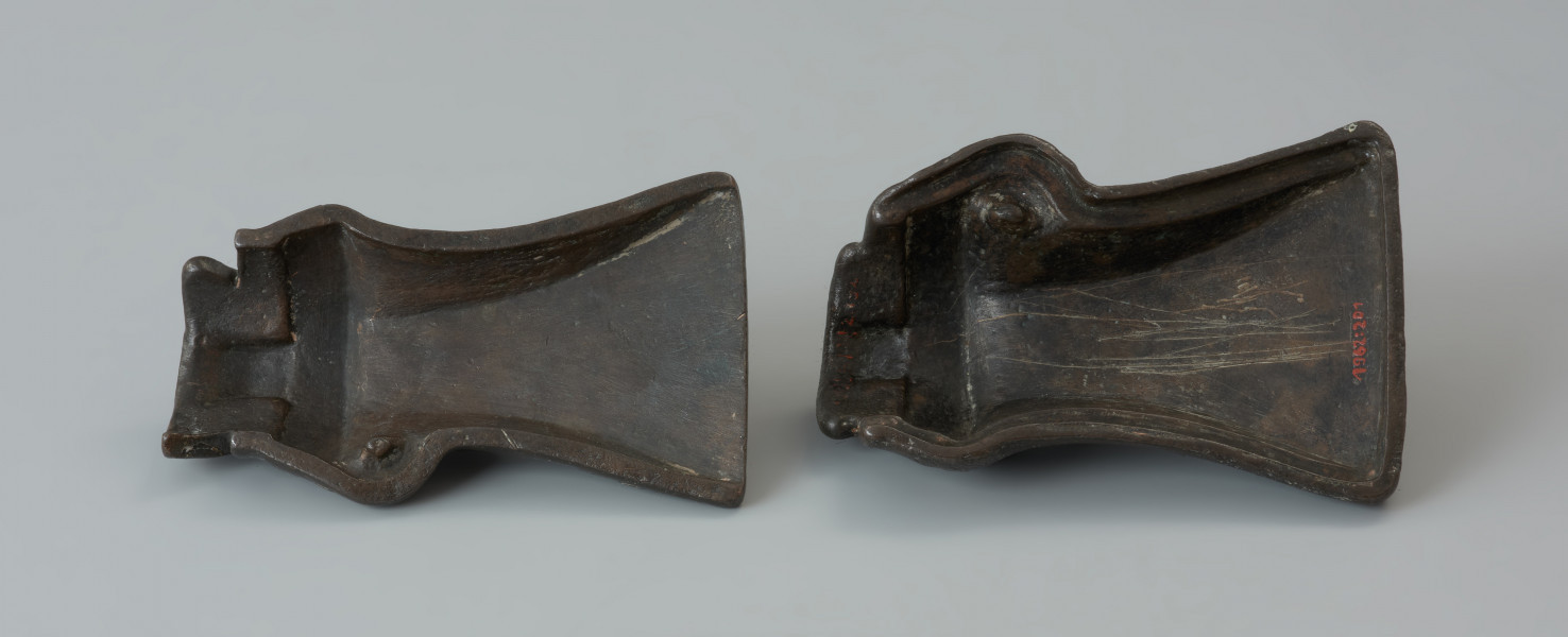 forma odlewnicza; forma muszlowata - Ujęcie wnętrza formy z góry. Dwuelementowa forma odlewnicza z brązu o brunatnozielonkawej barwie, której kształt wewnętrzny tworzy negatyw siekierki z tulejką i uszkiem. Połówki formy są do siebie dokładnie dopasowane, przy czym jedna zagłębia się lekko w drugiej. Wewnątrz ich korpusów znajdują się niewielkie wypustki w formie czopów, formujących uszko siekierki przy odlewaniu. Na ściankach zewnętrznych każdej połówki znajduje się uchwyt w postaci taśmowatego uszka. Powierzchnie te nie są gładkie a nieco porowate.