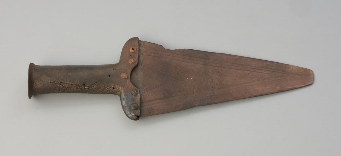 sztylet typu Orda-Łaba - Ujęcie spodniej części. Okazały sztylet z brązu charakteryzuje szerokie trójkątne ostrze zespolone przy pomocy pięciu nitów z masywną rękojeścią. Powierzchnia ostrza zdobiona jest motywem trójkąta.