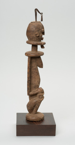 rzeźba - Ujęcie prawego boku. Drewniana, rzeźbiona Postać z dzieckiem na kolanach. Siedzi w pozycji przykucniętej. Głowa i tułów nieproporcjonalnie duże w stosunku do nóg. Oczy, nos, usta, uszy mocno wypukłe. Dziecko ułożone na kolanach, zasłania twarz rękoma. Na głowie fragment żelaza.