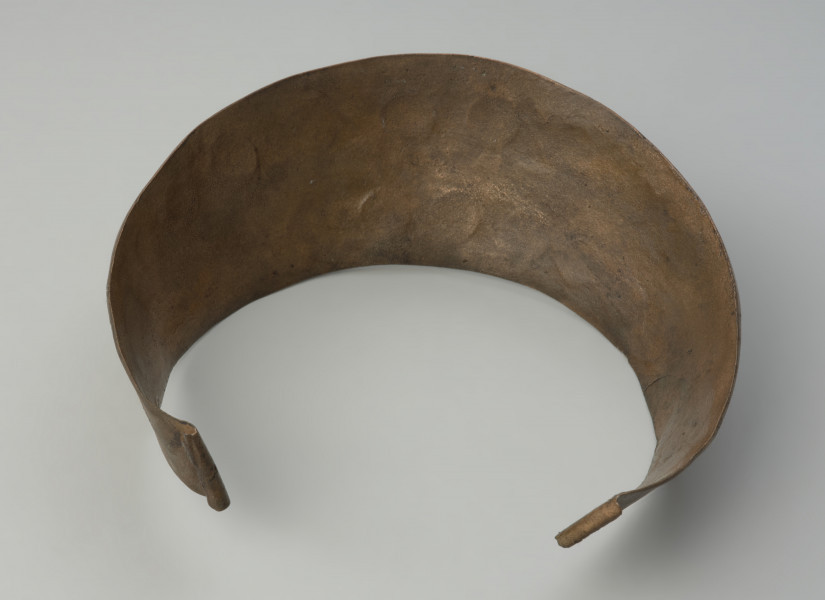 Brązowy naszyjnik kołnierzowaty - Ujęcie spodu naszyjnika. Brązowy naszyjnik kołnierzowaty jest zdobiony motywem  spiralnych pasm ułożonych w dwóch rzędach, oddzielonych podwójnym żeberkiem, ornamentowanym
drobnymi nacięciami i punktowaniem.