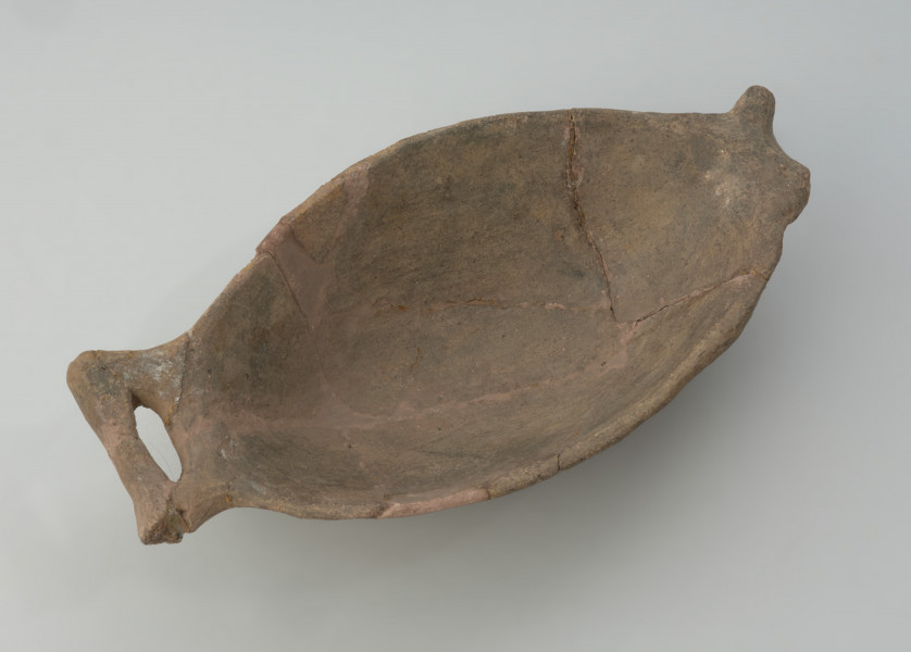 naczynie - Ujęcie pełne z góry. Płytka miseczka o oryginalnej formie, przypominającej kształtem rybę. Powierzchnia naczynia jest niezbyt starannie gładzona, barwa w tonacji szaro-brunatnej.