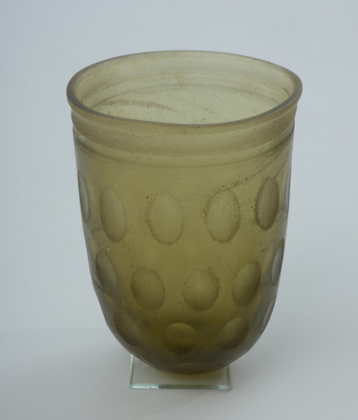 Naczynie szklane (pucharek) - Ujęcie z tyłu. Naczynie szklane (pucharek) grubościenne koloru jasnozielonego. Szkło jest przezroczyste.