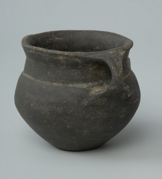 Ujęcie z boku. Niewielka brunatna waza gliniana o wygładzanej powierzchni.