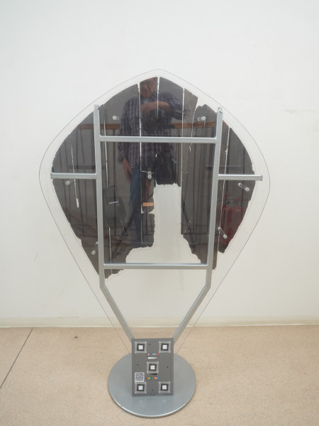 tarcza drewniana - Ujęcie z tyłu. Tarcza drewniana, nawiązująca do tarcz typu migdałowatego. Wykonana została z sześciu deszczułek, zwanych też plankami, o szerokości 6,5–17 cm i grubości 0,4–0,7 cm, ściśle przylegających do siebie, spojonych najpewniej klejem pochodzenia roślinnego (żywicznego) lub zwierzęcego (kostnego). Zachowała się jedynie drewniana część tarczy oraz lewy uchwyt skórzany, tak zwany imacz, w postaci paska skóry o długości 42 cm, który przymocowany był za pomocą gwoździ. Po prawym imaczu zachowały się jedynie otwory, podobnie jak po pasie naramiennym. Frontową powierzchnię tarczy pokrywają ślady kolorowej dekoracji namalowanej bezpośrednio na deszczułkach czerwoną, żółtą i czarną farbą. Część centralną zajmuje czerwono-żółty stylizowany krzyż o rozszerzających się ramionach. Wzdłuż brzegu widnieją czerwone kółka i czarne owale z żółtymi rozetami wewnątrz, układające się naprzemiennie, oddzielone od części centralnej czarną kreską.