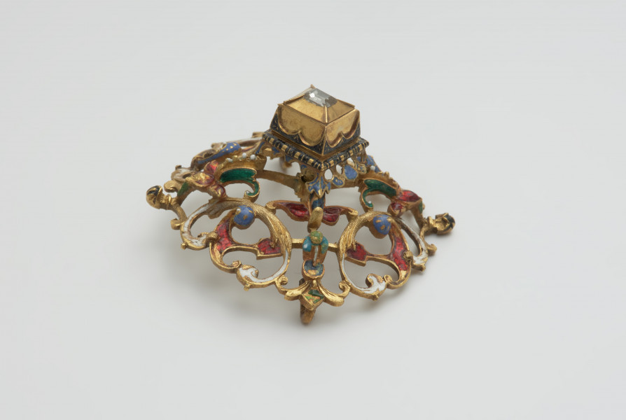 biżuteria, ozdoby - Ujęcie z boku z góry. Ażurowy klejnot z kołpaka z diamentem, zdobiony barwną emalią.