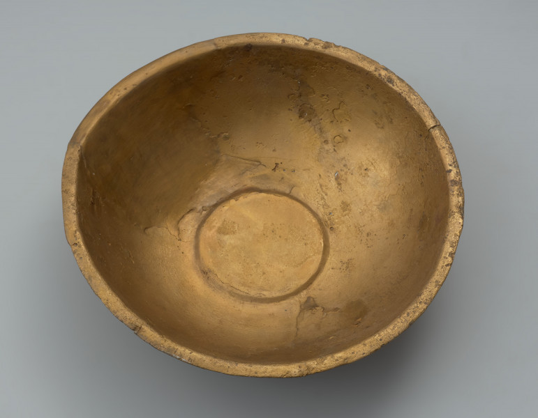 misa z rytem - Ujęcie z góry. Ozdobna misa wykonana została z jednego fragmentu blachy. Jej wąski, na zewnątrz wywinięty brzeg, miejscami opuszczony ku dołowi, ma zaokrągloną i lekko pogrubioną krawędź. Misa jest częściowo uszkodzona (jeden znaczny ubytek oraz kilkanaście mniejszych). Brakuje części ścianki od dna aż do wylewu. Pomimo ubytku i zniszczenia powierzchni zachowała się dekoracja ryta obejmująca wnętrze naczynia. Na nieco wklęsłym dnie widoczny jest duży medalion, z dodatkowo wydzieloną za pomocą podwójnej linii rytej częścią centralną wypełnioną liniami łamanymi. Na wewnętrznej powierzchni ścianki umieszczono symetrycznie cztery owalne medaliony z podobnym motywem, a pomiędzy nimi cztery 