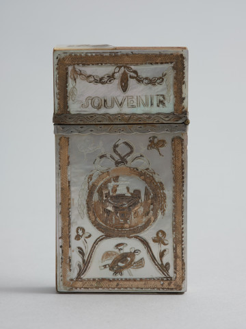 karnecik balowy - Ujęcie z przodu. Karnecik składa się z 4 prostokątnych płytek z kości słoniowej połączonych mosiężnym nitem. Górne krawędzie płytek zostały wycięte w kształt łuku wypukłego w części środkowej i wklęsłego po bokach.
Etui na karnecik ma formę płaskiego prostokątnego pudełka z pokrywą na zawiasie umieszczonym przy węższym boku. Drewniane pudełeczko obłożono płytkami z macicy perłowej z dekoracją rytą i złoconą, z motywami: wazy w okrągłym medalionie zwieńczonym kokardą, panopliów, kwiatów i motyli. Pokrywa po jednej stronie ozdobiona została girlandą i majuskułową inskrypcją: SOUVENIR (pamiątka), po drugiej elementem dekoracyjnym złożonym z owoców i liści oraz napisem: DAMITIE [d'amitié] (przyjaźń). Stykające się krawędzie pokrywy i pudełeczka okute srebrem z rytowanym wzorem.