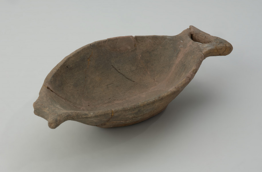 naczynie - Ujęcie z przodu skosem w lewą stronę. Płytka miseczka o oryginalnej formie, przypominającej kształtem rybę. Powierzchnia naczynia jest niezbyt starannie gładzona, barwa w tonacji szaro-brunatnej.