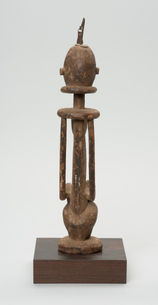 rzeźba - Ujęcie z tyłu. Drewniana, rzeźbiona Postać z dzieckiem na kolanach. Siedzi w pozycji przykucniętej. Głowa i tułów nieproporcjonalnie duże w stosunku do nóg. Oczy, nos, usta, uszy mocno wypukłe. Dziecko ułożone na kolanach, zasłania twarz rękoma. Na głowie fragment żelaza.