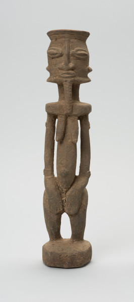 rzeźbiona figura - Ujęcie z przodu. Drewniana, rzeźbiona postać, z zaznaczonymi jednocześnie cechami płciowymi męskimi i żeńskimi. Wyodrębnione cechy męskie to broda, żeńskie: piersi.