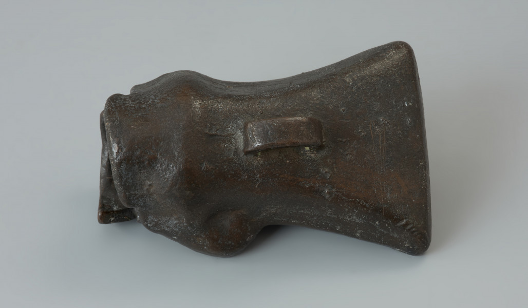 forma odlewnicza; forma muszlowata - Ujęcie w poziomie jednego elementu formy. Dwuelementowa forma odlewnicza z brązu o brunatnozielonkawej barwie, której kształt wewnętrzny tworzy negatyw siekierki z tulejką i uszkiem. Połówki formy są do siebie dokładnie dopasowane, przy czym jedna zagłębia się lekko w drugiej. Wewnątrz ich korpusów znajdują się niewielkie wypustki w formie czopów, formujących uszko siekierki przy odlewaniu. Na ściankach zewnętrznych każdej połówki znajduje się uchwyt w postaci taśmowatego uszka. Powierzchnie te nie są gładkie a nieco porowate.