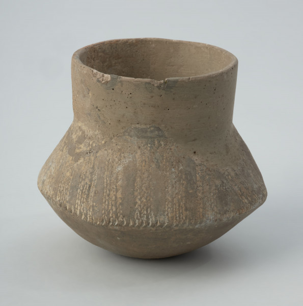 Naczynie gliniane - Ujęcie z przodu; Naczynie wazowate o dwustożkowatym brzuścu, pionowej szyjce i niewyodrębnionym dnie. Brzusiec o zarysie czworobocznym w rzucie z góry. Zdobione w górnej części brzuśca ukośnymi pasmami złożonymi z 3 podwójnych linii kreskowo-kłutych wykonanych dwuzębnym narzędziem. Pasma trzykrotnie zmieniają kierunek nachylenia, tworząc układ krokwiasty. Cały układ podkreślony dookolnym pasmem odcisków paznokcia na załomie brzuśca. Szyjka naczynia, niemal w całości zrekonstruowana, prawdopodobnie nie była zdobiona, podobnie jak dół brzuśca