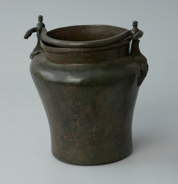 Ujęcie z przodu. Situla (wiadro) z brązu z tzw. ataszami w postaci stylizowanych postaci delfinów.