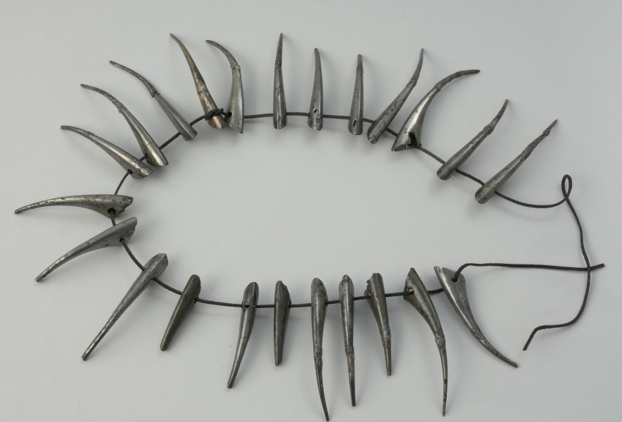 wisior, biżuteria, naszyjnik, kolia, ozdoba ciała - Ujęcie z góry przodu kolii. Kolia z wisiorków wykonanych z tzw. białego brązu. Każdy o formie wydłużonego rożka z wygiętym kolcem, ściętą ukośnie krawędzią podstawy oraz parą otworów.