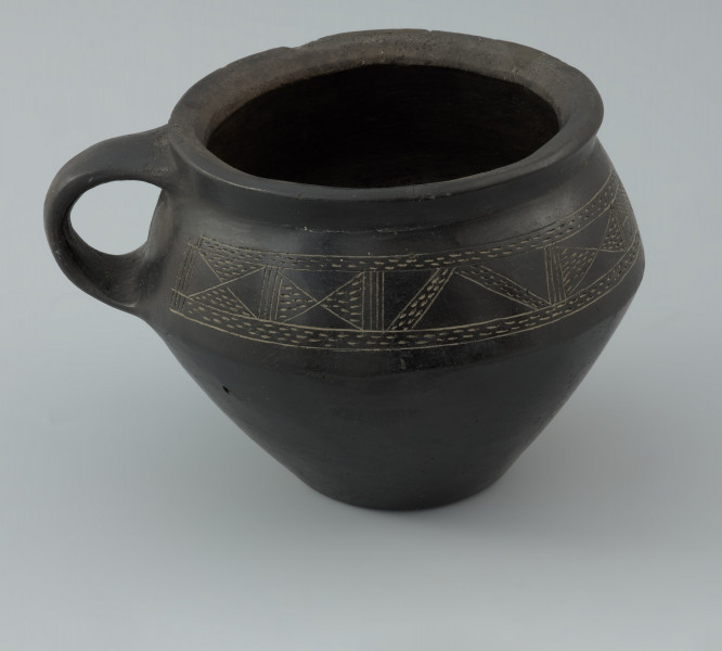 Naczynie gliniane - Ujęcie prawego boku. Naczynie gliniane (kubek) posiada gładką, czarną powierzchnię i drobną domieszkę.