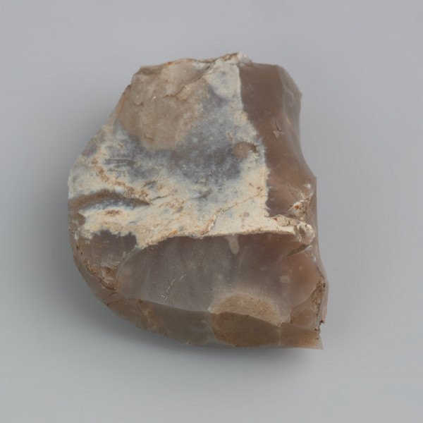 Rdzeń wiórowy podstożkowy - ujęcie z przodu; Płaski, tabliczkowaty rdzeń jednopiętowy, eksploatowanym przy pomocy pośrednika, o czym świadczą płaskie, rozlane sęczki oraz słabo widoczne fale odbić na negatywach po odbitych odłupkach. Pięta rdzenia uformowana jest wieloma krótkimi odbiciami. Na jednej ze ścianek zachowana jest jasna, biaława kora. Tył rdzenia naturalny (niemodyfikowany). Powierzchnia rdzenia jest silnie wyświecona na skutek długotrwałego zalegania na powierzchni.