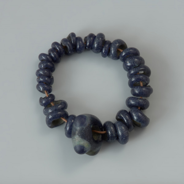 Bransoletka z paciorków szklanych - Ujęcie z góry całej bransoletki; Zbiór 28 niewielkich paciorków szklanych i jednego większego, najprawdopodobniej tworzących jedną bransoletkę.