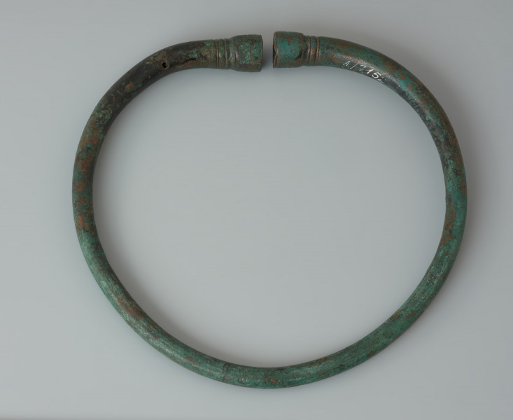 Naszyjnik z pogrubionymi zakończeniami wykonany z brązu - ujęcie z góry od tyłu. Naszyjnik z pogrubionymi zakończeniami wykonany z brązu. Ornament krzyża na zakończeniach nosi ślady czerwonej emalii.