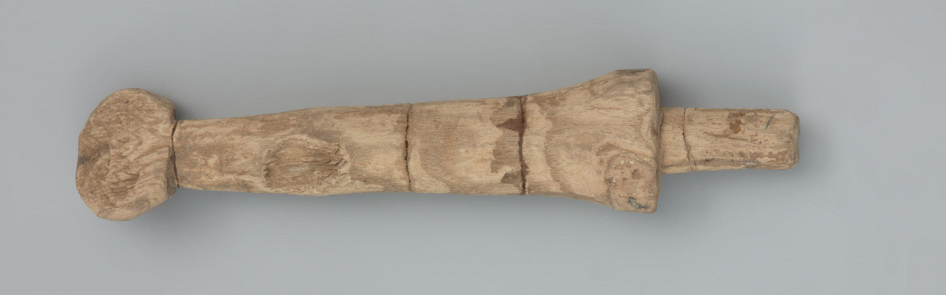 Mieczyk drewniany - Ujęcie tyłu z góry.  Drewniany mieczyk-zabawka z okrągłą głowicą kończącą lekko zwężoną rękojeść, bez jelca, z głownią płaską, ułamaną .