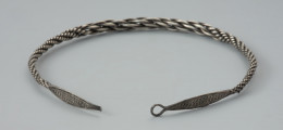 naszyjnik srebrny - Ujęcie zapięcia naszyjnika. Naszyjnik srebrny z czterech par skręconych drutów owijanych wokół siebie o grubości całkowitej od 0,4 do 1 cm. W części środkowej druty są skręcone zdecydowanie luźniej, co powoduje, że obręcz jest w tym miejscu grubsza. Oba końce obręczy są rozklepane w wydłużone owalne płytki zakończone uszkiem i haczykiem (fragment odłamany). Płytki są zdobione bordiurą z płaskich granulek wzdłuż obu krawędzi oraz dwoma rzędami trójkątów z trzema płaskimi granulkami w każdym z nich.