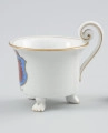 filiżanka w kształcie cylindrycznym - Ujęcie prawej strony. Filiżanka z białej porcelany o kształcie cylindrycznym, rozszerzającym się ku górze, na trzech nóżkach w formie łap zwierzęcych. Uszko wolutowe wysunięte ponad czarkę w obrębie zawinięcia woluty przymocowanej dołem do krawędzi czarki. Kształt uszka podkreślony w środku i na bocznych krawędziach złotym paskiem. Na ściance podszkliwna dekoracja - barwny herb Szczecina - niebieska tarcza ze złotym obrzeżem, o ściętych narożnikach, zwieńczona sepiowo-brązową koroną muralis. Wewnątrz tarczy czerwona głowa gryfa z czarnym rysunkiem piór, ze złotą koroną. Krawędź czarki opracowana złotą lamówką, powtórzoną wąskim paskiem wokół wewnętrznej krawędzi czarki. Nóżki, na których opiera się czarka, wyprofilowane w poczwórne pazury podkreślone złotym akcentem.