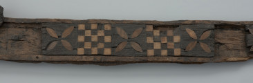 szkatułka intarsjowana - Ujęcie drugiego fragmentu szkatułki. Fragment wieko szkatułki z drewna bukowego, intarsjowana drewnem dębowym i cisowym.  Przybrzeżną część ścianki otacza kompozycja złożona z naprzemiennie umieszczanych motywów: szachownic o 25 polach i czterolistnych rozet z jasnego drewna, precyzyjnie wkomponowanych w soczewkowate wycięcia w płycinach z ciemniejszej dębiny.