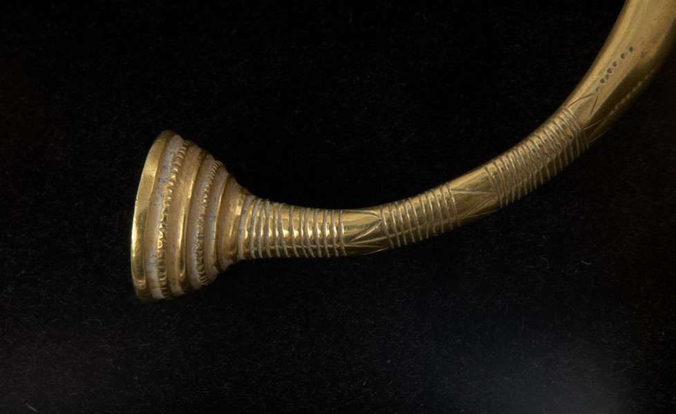 bransoleta z pieczątkowatymi zakończeniami - Ujęcie detalu zapięcia z prawej strony. Bransoleta złota z pieczątkowatymi zakończeniami, którą zdobi żebrowanie, grupy nacięć oraz zygzaki.