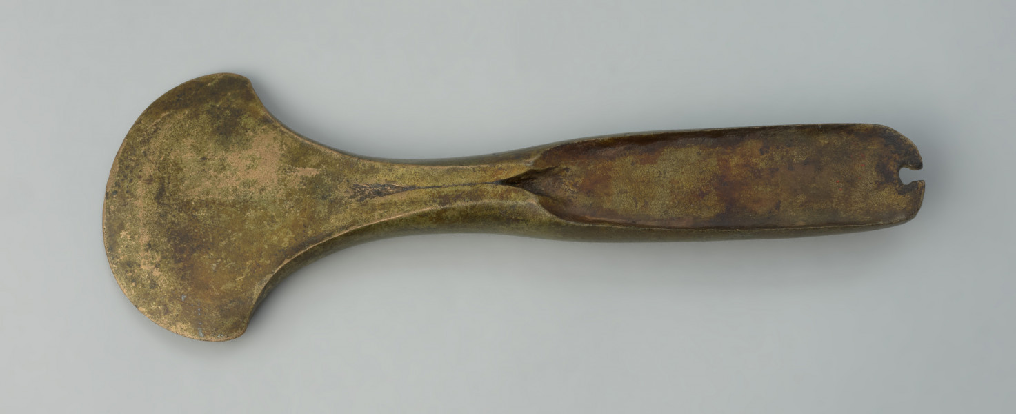 siekierka z piętką - Ujęcie z góry przodu siekierki. Siekierka brązowa o zabawieniu złocistym z lejkowatą piętką i wąskim, łukowato zakończonym obuchem, na szczycie którego widnieje wyraźna wnęka. Ostrze zostało uformowane wachlarzowato.