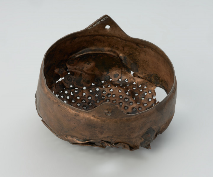 Cedzak ze stopu miedzi - Ujęcie z góry prawego boku. Cedzak ze stopu miedzi o owalnym kształcie z dwoma trójkątnymi uchami.