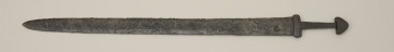 broń; miecz dwusieczny - Ujęcie przodu miecza. Całkowicie zachowany. Dwusieczna głownia jest szeroka i masywna, o mniej więcej jednakowej szerokości na całej długości, przy zastawie ma przekrój sześcioboczny. Sztych jest zaokrąglony. Na obu płazach głowni widoczny wzór w postaci „jodełki” świadczący o wieloelementowej jej konstrukcji. Rdzeń został wykonany z dwóch skręconych prętów, nisko- i wysokowęglowego, tworzących jądro, z dodanymi po obu stronach nakładkami ostrzy. Trzpień miecza jest wąski i lekko zwęża się ku głowicy. Jelec jest krótki i wysoki, o kształcie widzianym od góry zbliżonym do prostokąta o lekko wypukłych krótszych bokach. Głowica jest jednolita, zbliżona do trójkąta. Jelec i głowica są lite, wykute każde z pojedynczego kawałka metalu.
