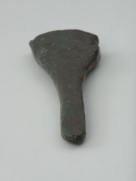 Trzewik pochwy miecza - Ujęcie spodu trzewika pochwy miecza w pionie. Niezdobiony trzewik pochwy miecza o formie niewielkiego, silnie spłaszczonego lejka, którego powierzchnia jest nierówna i porowata, a krawędź jego nasady uszkodzona.