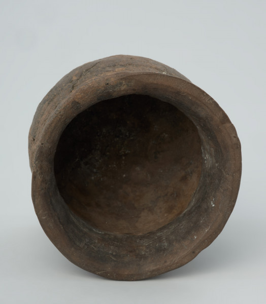 Naczynie gliniane - Ujęcie wnętrza.  Puchar o kształcie esowatym, być może pierwotnie zaopatrzony w ucho, zdobiony na szyjce dookolnym pasmem złożonym z 10 rzędów ornamentu odcisków sznura. Naczynie zrekonstruowane na podstawie drobnych fragmentów wylewu, szyjki, brzuśca i dna, uzupełnione barwionym gipsem. Powierzchnia szarobrunatna, z powierzchnią niedokładnie wyrównaną. W masie, na powierzchni widoczna domieszka mineralna.