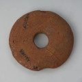 zawieszka, amulet - Ujęcie z góry spodu tarczki. Tarczka bursztynowa w formie dysku z niewielkim otworem pośrodku o spatynowanej i popękanej powierzchni.