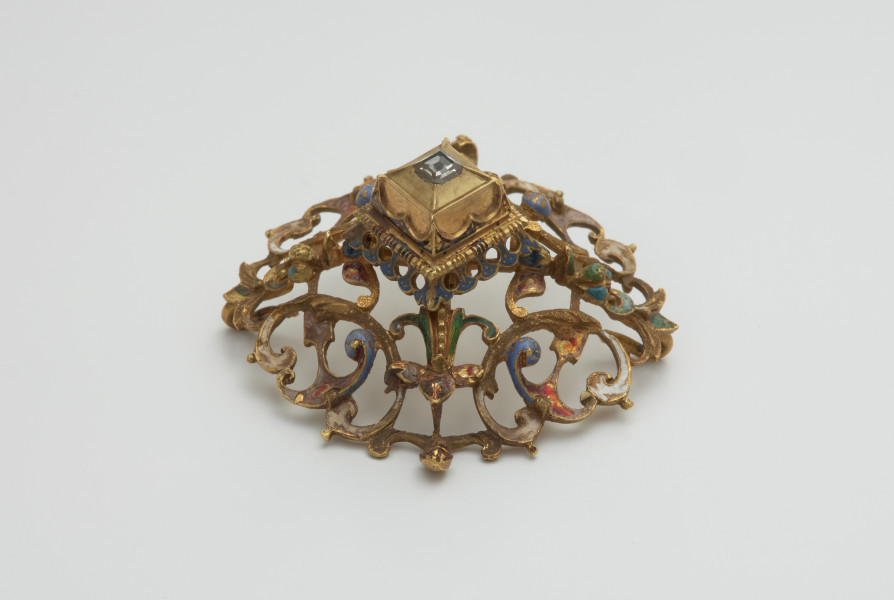 biżuteria, ozdoby - Ujęcie z boku z lewej strony. Ażurowy klejnot z kołpaka z diamentem, zdobiony barwną emalią.