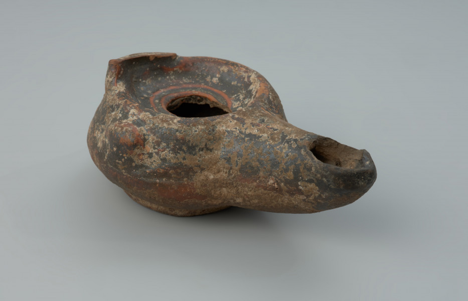 Rzymska lampka oliwna z gliny z urwanym uchem - Ujęcie z przodu z prawej strony. Rzymska lampka oliwna z gliny z urwanym uchem.