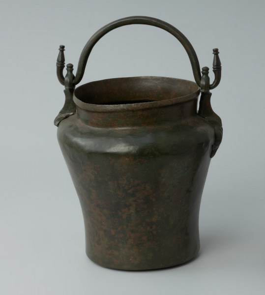 Ujęcie z przodu z podniesioną rączką. Situla (wiadro) z brązu z tzw. ataszami w postaci stylizowanych postaci delfinów.
