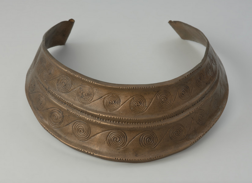 Brązowy naszyjnik kołnierzowaty - Ujęcie z przodu. Brązowy naszyjnik kołnierzowaty jest zdobiony motywem  spiralnych pasm ułożonych w dwóch rzędach, oddzielonych podwójnym żeberkiem, ornamentowanym
drobnymi nacięciami i punktowaniem.