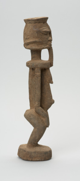 rzeźbiona figura - Ujęcie prawego boku. Drewniana, rzeźbiona postać, z zaznaczonymi jednocześnie cechami płciowymi męskimi i żeńskimi. Wyodrębnione cechy męskie to broda, żeńskie: piersi.