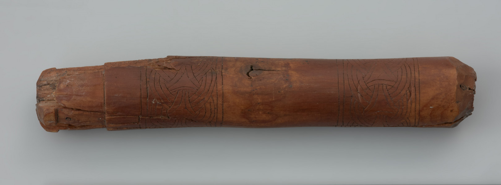 nóż z rękojeścią - Ujęcie z przodu.  Uszkodzony nóż żelazny zachował się wraz z oprawką zdobioną motywami ze sztuki skandynawskiej. Końcówka trzpienia noża została zawinięta w uszko. Drewniana oprawka jest dekorowana w stylu skandynawskim okresu wikingów. Pasmowo rozmieszczone wątki dekoracyjne znajdujące się w dolnej części całego motywu ornamentacyjnego kojarzą się z mocno zgeneralizowanym splotem sznurowym. Krzyż wpisany w okrąg, znajdujący się w centralnej części motywu przypomina rozwiązania znane ze stylu Borre, ale też wykazuje podobieństwa do ornamentyki określanej mianem Jellinge i Mammen.