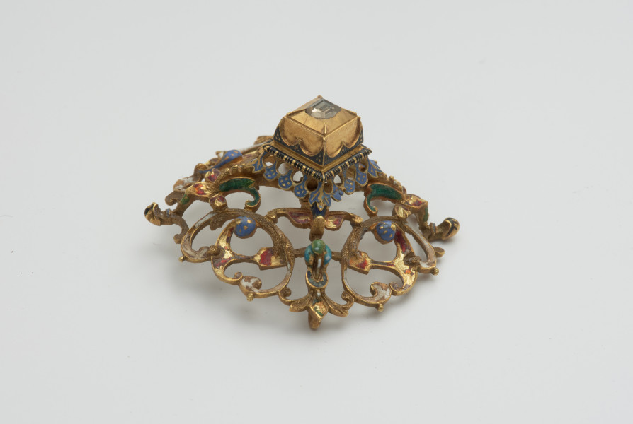 biżuteria, ozdoby - Ujęcie z boku z góry. Ażurowy klejnot z kołpaka z diamentem, zdobiony barwną emalią.